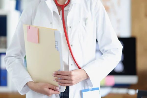 Női orvos fehér köpenyben és sztetoszkóppal orvosi dokumentumokat tart a kezében. — Stock Fotó