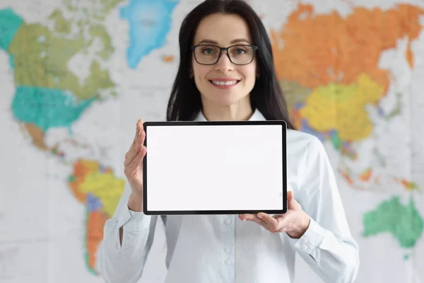Mujer sonriente en gafas sostiene tableta con pantalla blanca en blanco en el fondo del mapa global del mundo —  Fotos de Stock