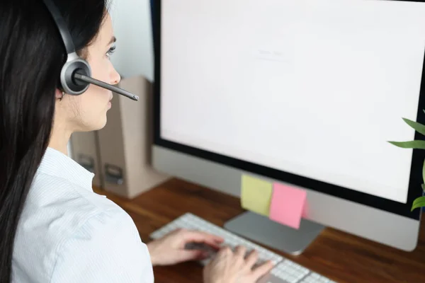 Mulher consultora em fones de ouvido com microfone senta-se na frente do monitor do computador. — Fotografia de Stock