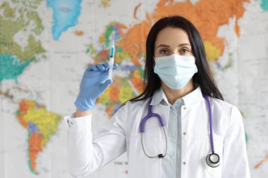 Koruyucu tıbbi maskeli kadın doktor dünya haritasının arka planında aşılı şırınga tutuyor.