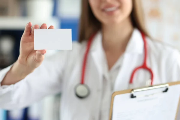 Female doctor is holding white business card in front of her medical office