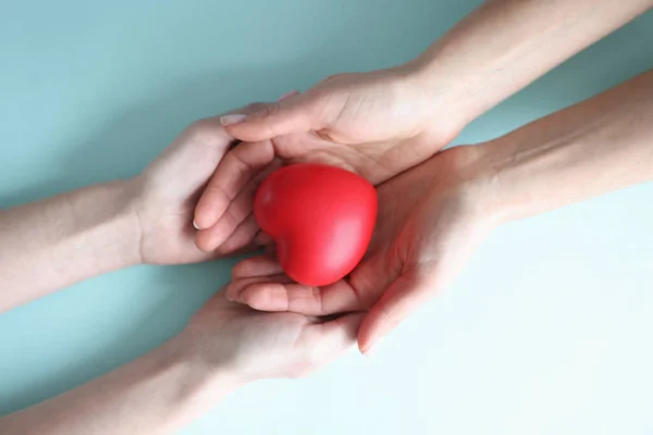 Małe czerwone serce leży w rękach dwojga ludzi — Zdjęcie stockowe