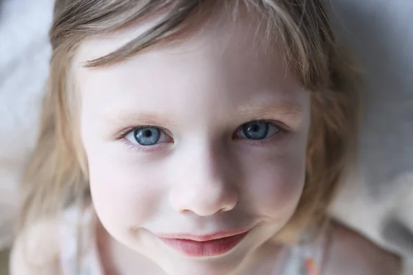 Portrét usměvavé holčičky s modrýma očima v posteli — Stock fotografie