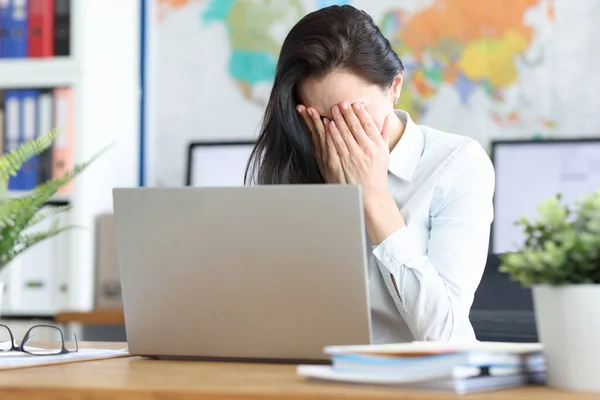 Triste giovane donna siede al computer portatile coprendo il viso con le mani — Foto Stock