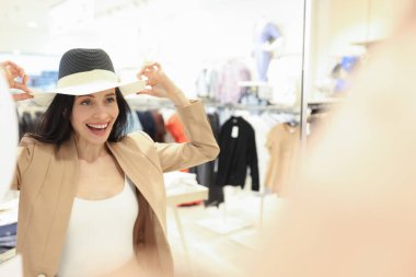 Duygusal olarak gülümseyen bir kadın aynanın önünde şapka takmaya çalışır.