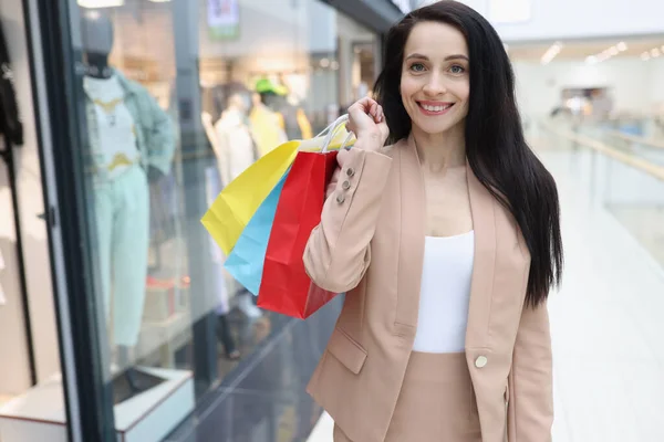 Donna sorridente in abito da lavoro sta nel centro commerciale con sacchetti di carta shopping — Foto Stock