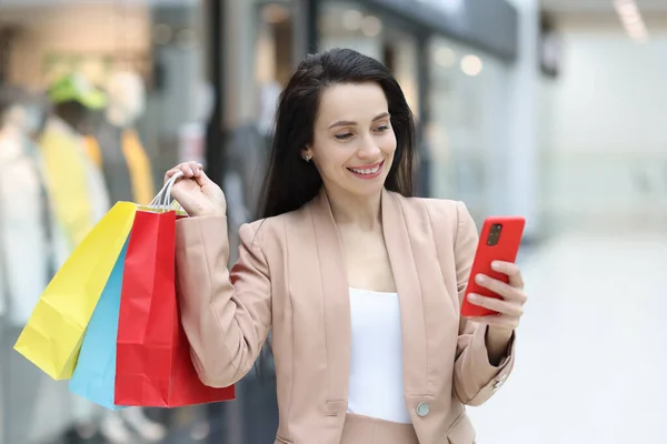 Donna sorridente tiene in mano smartphone e acquisti nel centro commerciale — Foto Stock