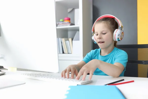 Menina em fones de ouvido senta-se no monitor de computador e tipos no teclado — Fotografia de Stock