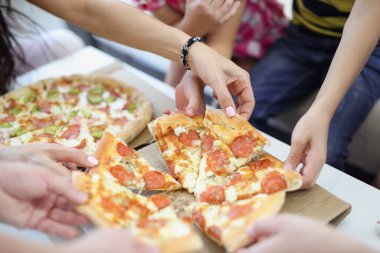 Çocukların ve ailelerin elleri pizzayı yakın plan çekiyorlar.