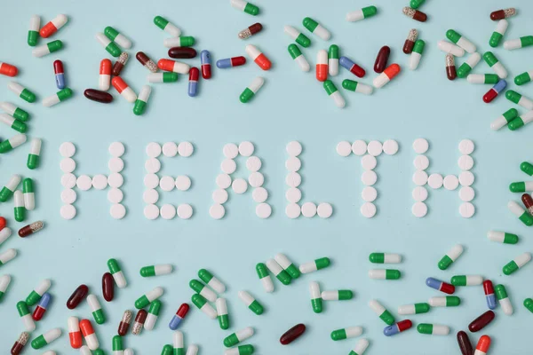 La salud de la palabra se establece a partir de píldoras blancas en el fondo de cápsulas multicolores fondo de primer plano — Foto de Stock