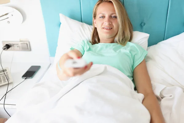 Jovem deitada na cama com TV controle remoto em suas mãos — Fotografia de Stock