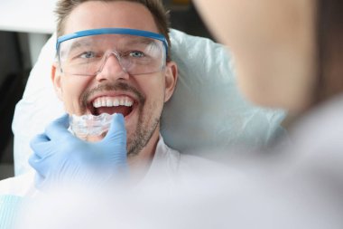 Doktor, gülümseyen genç adamın doğru ısırması için plastik ağız koruyucusu dener.