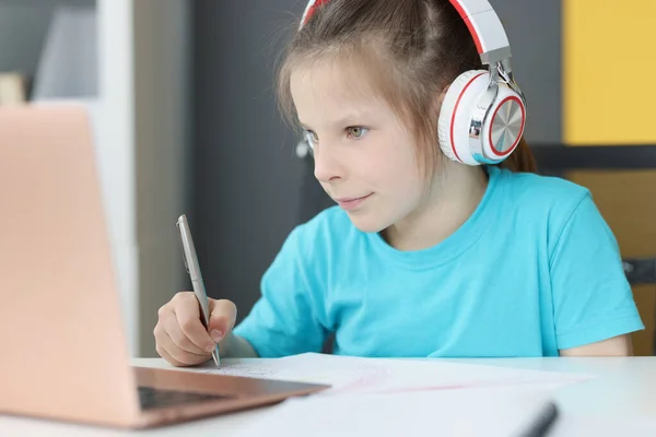 Petite fille préscolaire dans les écouteurs assis au bureau d'étude en ligne sur ordinateur portable — Photo
