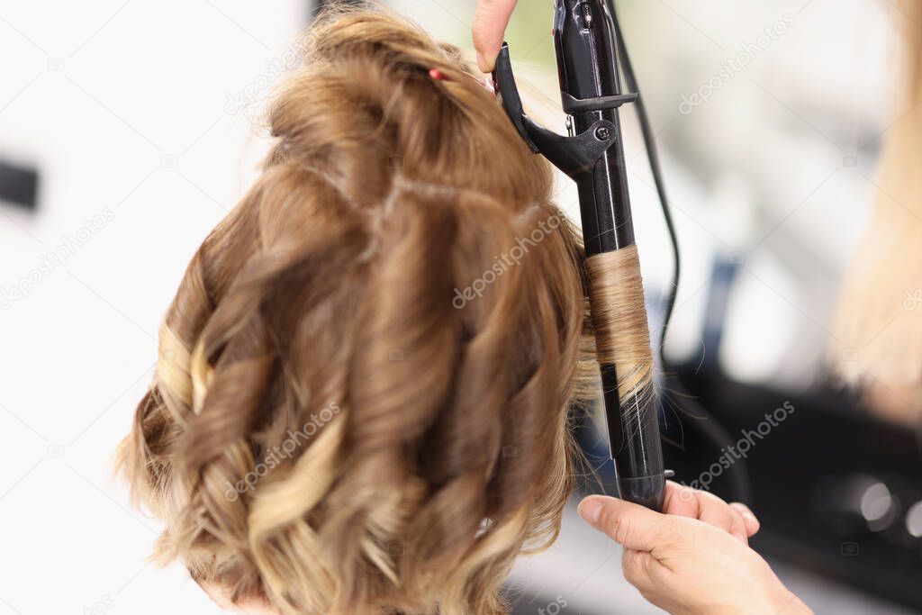 Hairdresser makes evening hairstyle for woman in form of curls