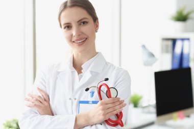 Medine ofisinde steteskop tutan beyaz önlüklü genç kadın doktor portresi.