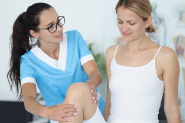 Kadın doktor, hastanın diz eklemini muayene ediyor.