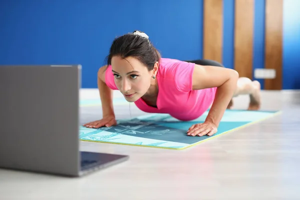 Жінка в спортивному одязі, стоячи на дошці на підлозі перед ноутбуком — стокове фото