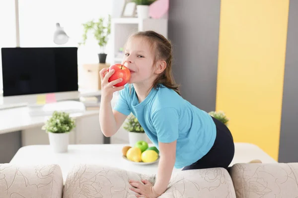 Menina sentada no sofá e comer maçã vermelha em casa — Fotografia de Stock