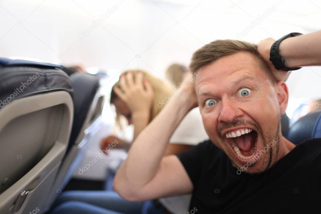 Male passenger holding his head and shouting on plane