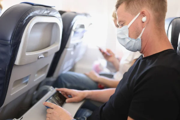 Hombre con máscara de protección médica se sienta en el avión y ve el vídeo en su teléfono inteligente — Foto de Stock