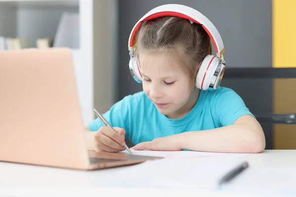 Petite fille dans des écouteurs étudiant à la maison devant un ordinateur portable à la maison — Photo