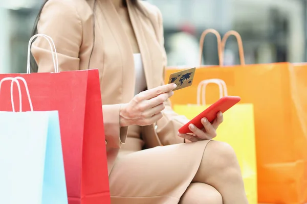 Mujer sosteniendo teléfono móvil y tarjeta bancaria de crédito cerca de bolsas de compras multicolores primer plano —  Fotos de Stock