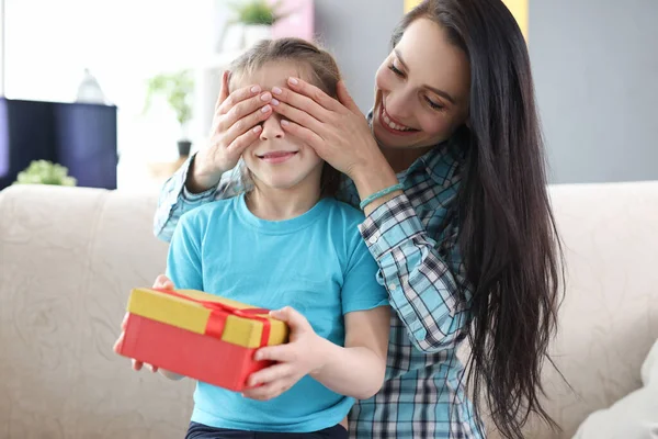 Mutter bedeckt die Augen ihrer Tochter mit den Händen. Kleines Mädchen hält Schachtel mit Geschenk — Stockfoto