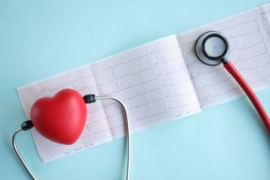 Stetoskop ve kırmızı oyuncak kalp mavi arka planda elektrokardiyogramda yatıyor.