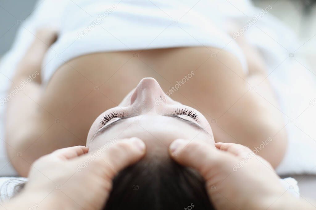 Young woman masseur makes face and head massage in spa salon