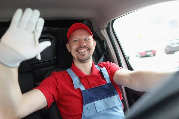 Smiling male courier driver waves his hand while driving