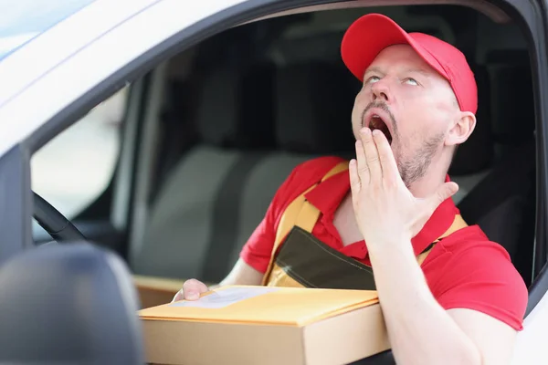 Young male courier driver yawns while driving car