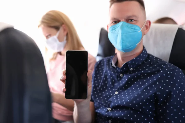 Porträtt av människan i medicinsk skyddsmask i flygplanskabinen framför subwoofer håller smartphone — Stockfoto