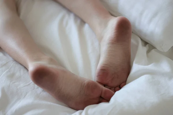 Sucios pies masculinos yacen en la cama blanca limpia —  Fotos de Stock
