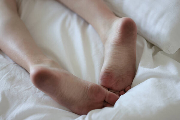 Dirty male feet lie on clean white bed