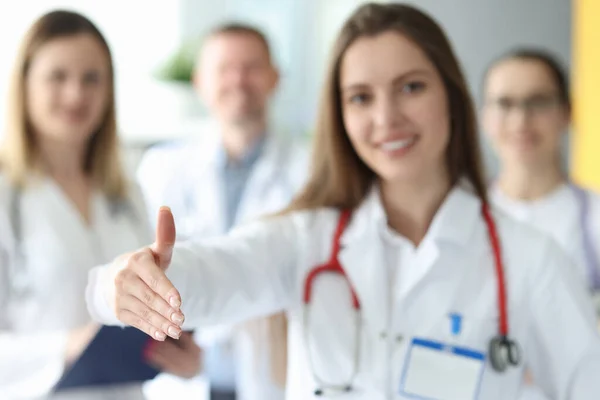 Mujer médico dando la mano para apretón de manos en el fondo de los colegas en primer plano de la clínica —  Fotos de Stock