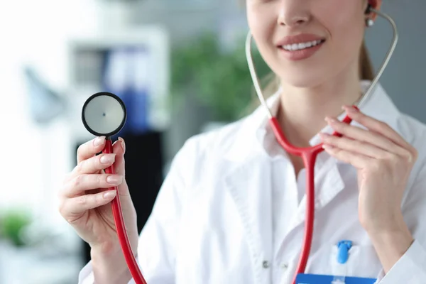 Young woman doctor holding red stethoscope in clinic closeup — Stock Photo, Image