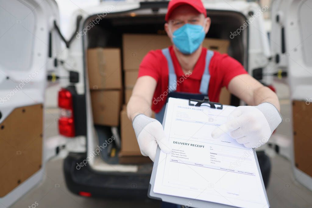 Male courier in protective mask pointing with finger where to sign on delivery receipt closeup
