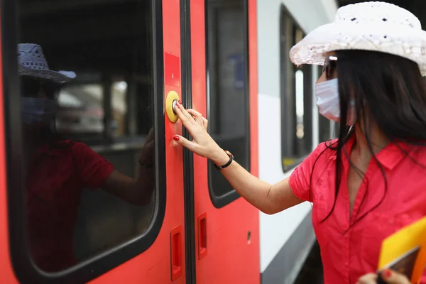 Koruyucu tıbbi maskeli kadın turist, tren kapısını açmak için düğmeye basıyor. — Stok fotoğraf