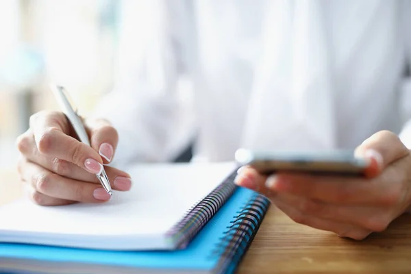 Woman hand holds smartphone in her hand and makes notes in notebook