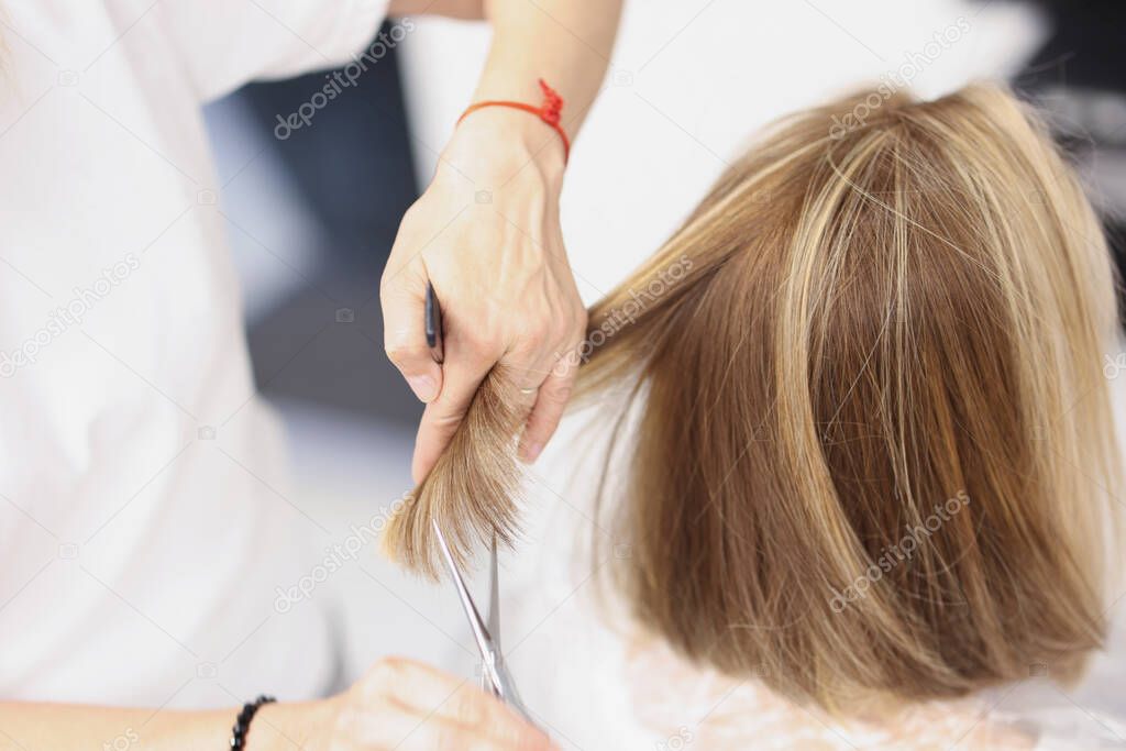 Master hairdresser cuts ends of a client hair in beauty salon