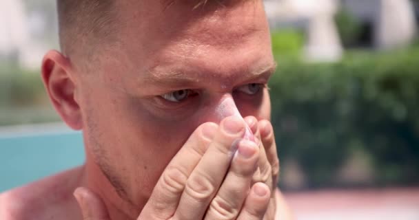 Jongeman smeren gezicht met zonnebrandcrème op het strand 4k film — Stockvideo