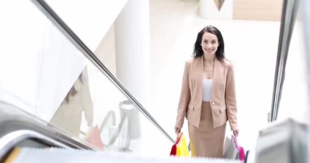 Mujer feliz montando escaleras mecánicas en el centro comercial con muchas bolsas de colores en sus manos 4k película — Vídeos de Stock