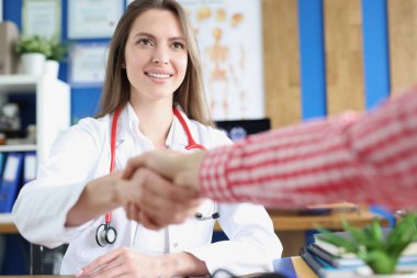 Gülümseyen beyaz kadın doktor selamlaşmak ve hastayla hastanede buluşmak için el sıkışıyor.