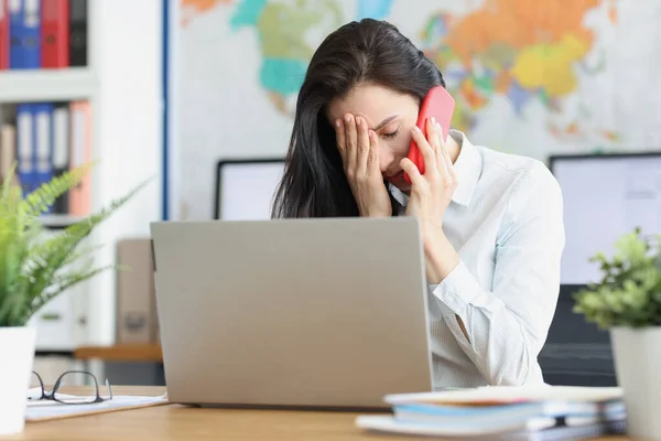 Upset young woman talking on smartphone while sitting at workplace — Stock Photo, Image