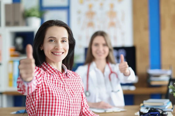 Zufrieden lächelnde junge erwachsene Patientin zeigt gemeinsam mit Arzt Daumen hoch — Stockfoto