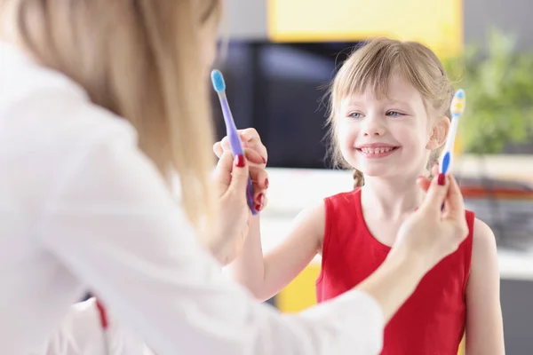 Zahnarzt bietet kleinem Mädchen in Klinik zwei Zahnbürsten zur Auswahl an — Stockfoto