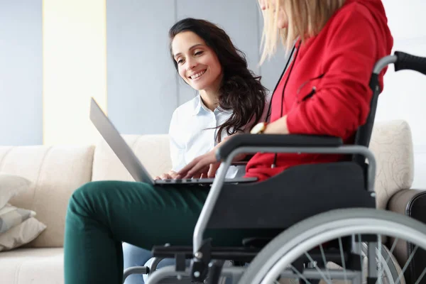 Інвалідність жінка в інвалідному візку і її друг дивиться на екран ноутбука вдома — стокове фото