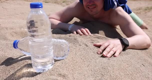 L'homme déshydraté atteint la bouteille d'eau tout en étant allongé sur du sable film 4k — Video