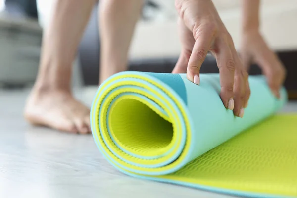Woman folds yoga or fitness mat after workout at home in living room — Stockfoto