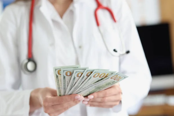 Doutor segurando lotes de notas de dólar em suas mãos em closeup clínica — Fotografia de Stock
